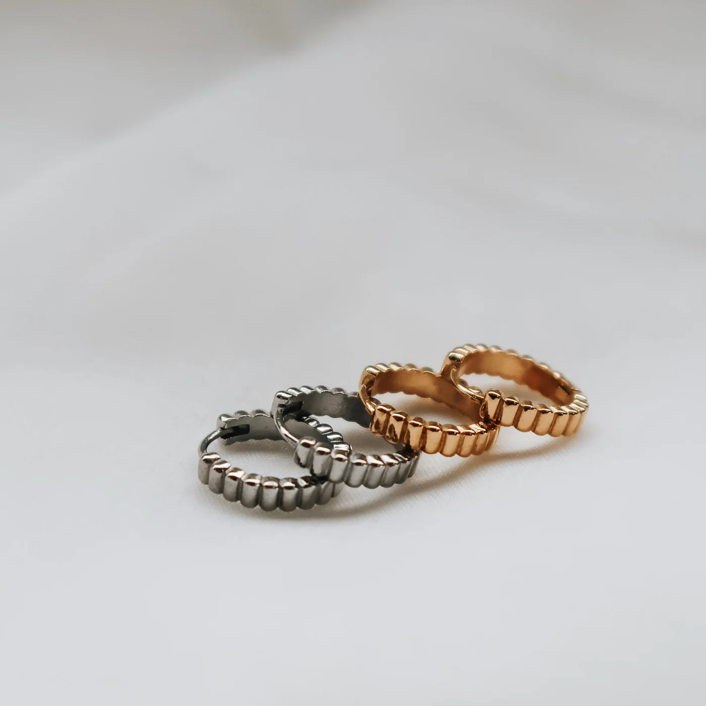 Ribbed hoop earrings in gold and silver,  on a light gray background